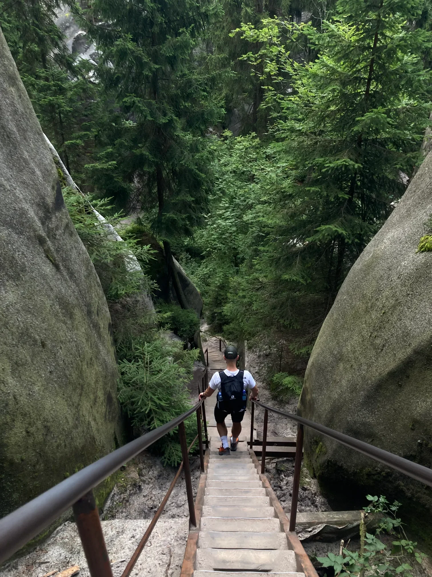 Turista stoupající po strmých schodech s kovovým zábradlím mezi pískovcovými skalami v létě v Adršpašských skalách