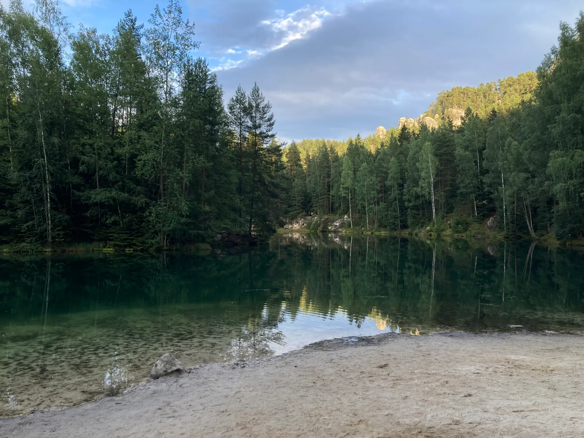 Smaragdové jezero v Adršpašských skalách v létě, písčité břehy a odrazy stromů v klidné hladině