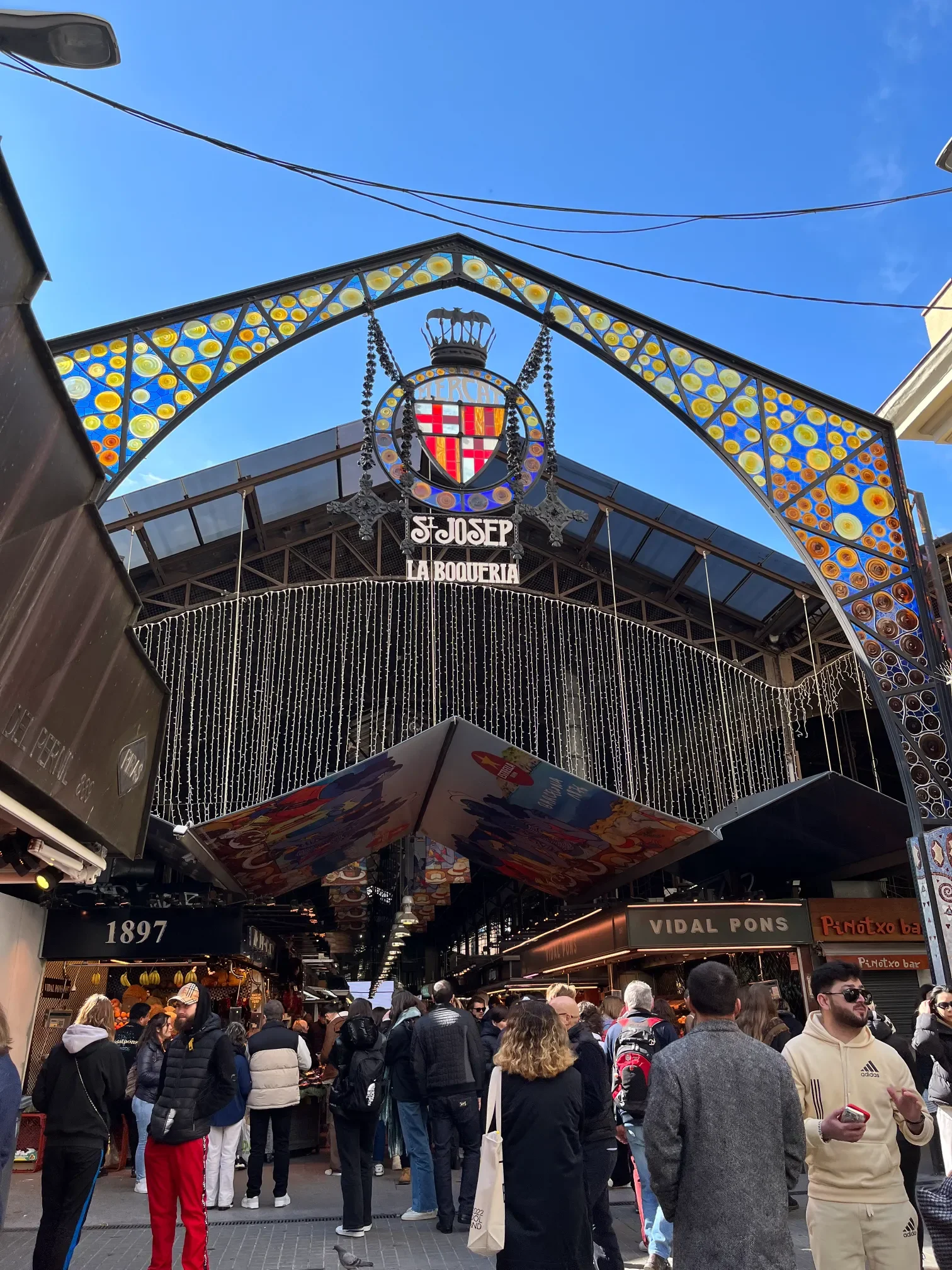 Secesyjny wejściowy łuk targu La Boqueria przy La Rambli w Barcelonie z kolorowym witrażem i tłumem turystów