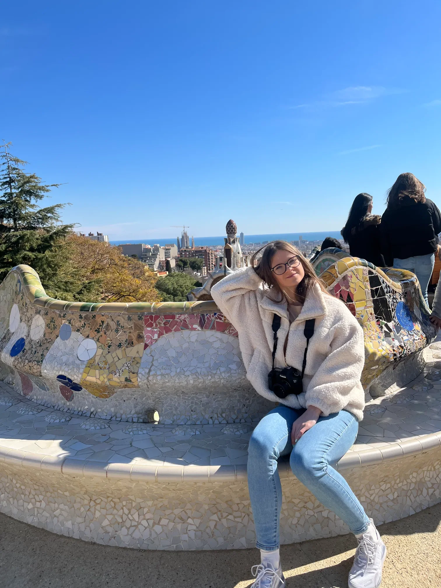 Turystka na falującej ławce z mozaiki trencadís na tarasie Park Güell w Barcelonie z panoramą miasta w tle