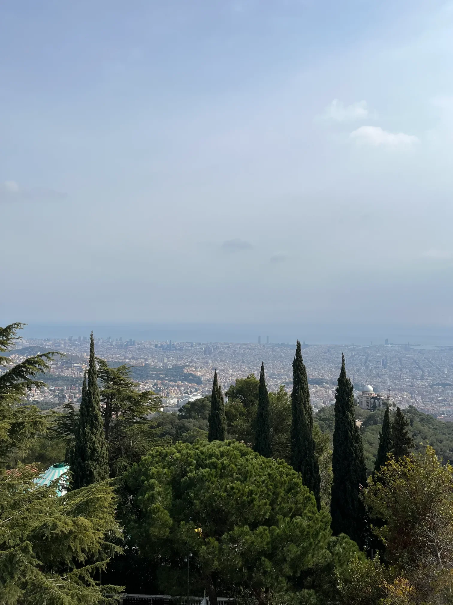 Panorama Barcelony i morza widziana ze wzgórza Tibidabo między smukłymi cyprysami