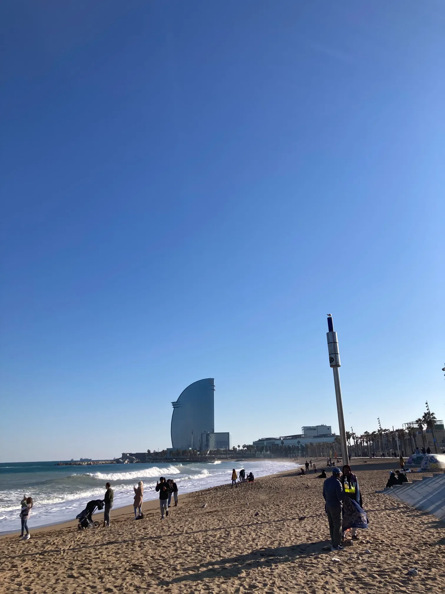 Plaża Barceloneta w Barcelonie z żaglokształtnym hotelem W nad morzem i spacerowiczami na piasku
