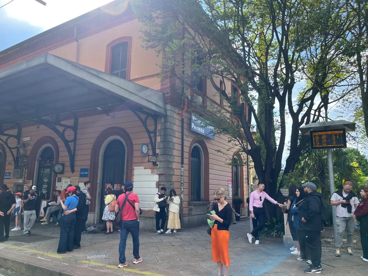 Historická budova vlakové stanice Varenna-Esino Perledo s turisty čekajícími na nástupišti u jezera Como