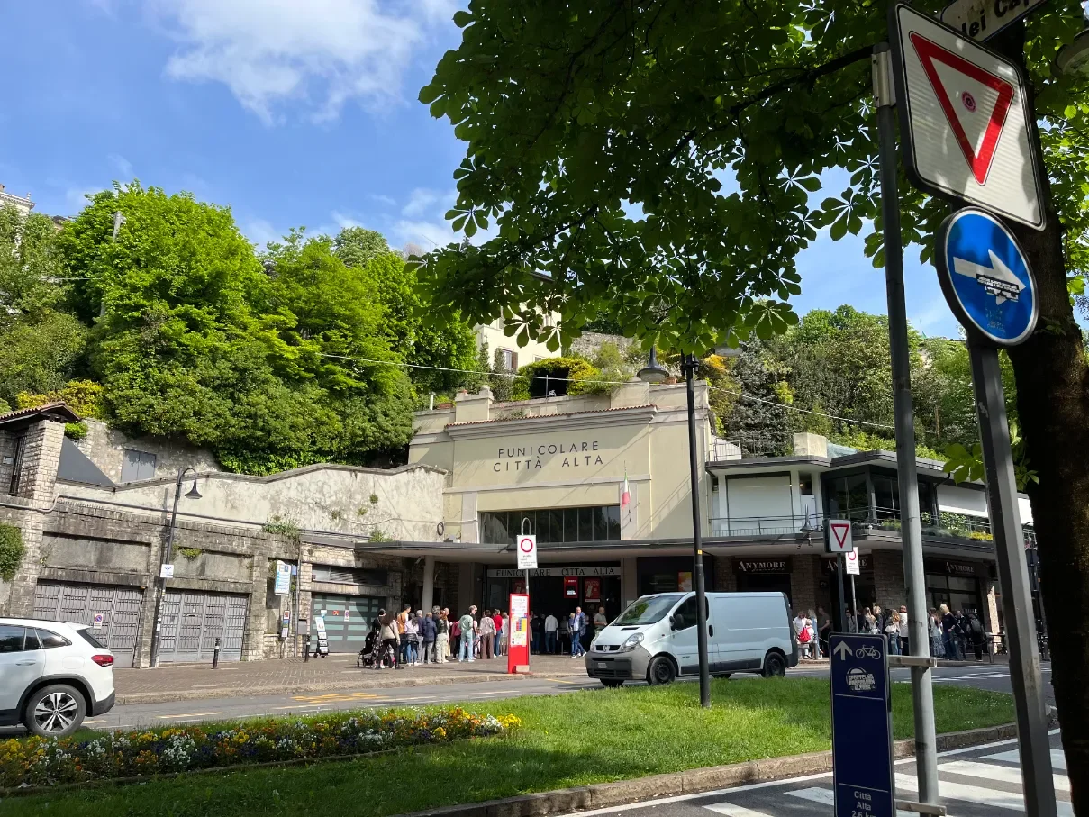 Stanice lanovky Funicolare Città Alta v Bergamu s frontou lidí a kvetoucím kaštanem, slunečný den
