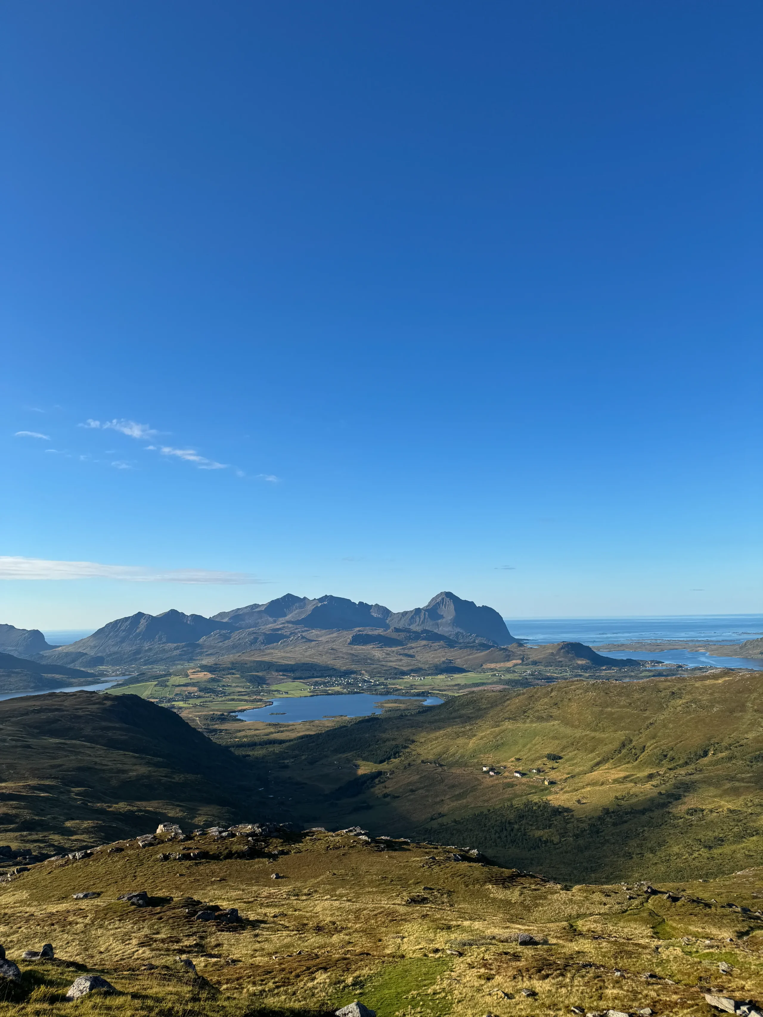 Panorama z hřebene Blåtinden na jezera v údolí Vestvågøya a skalnaté vrcholy Lofot za slunečného podzimního dne