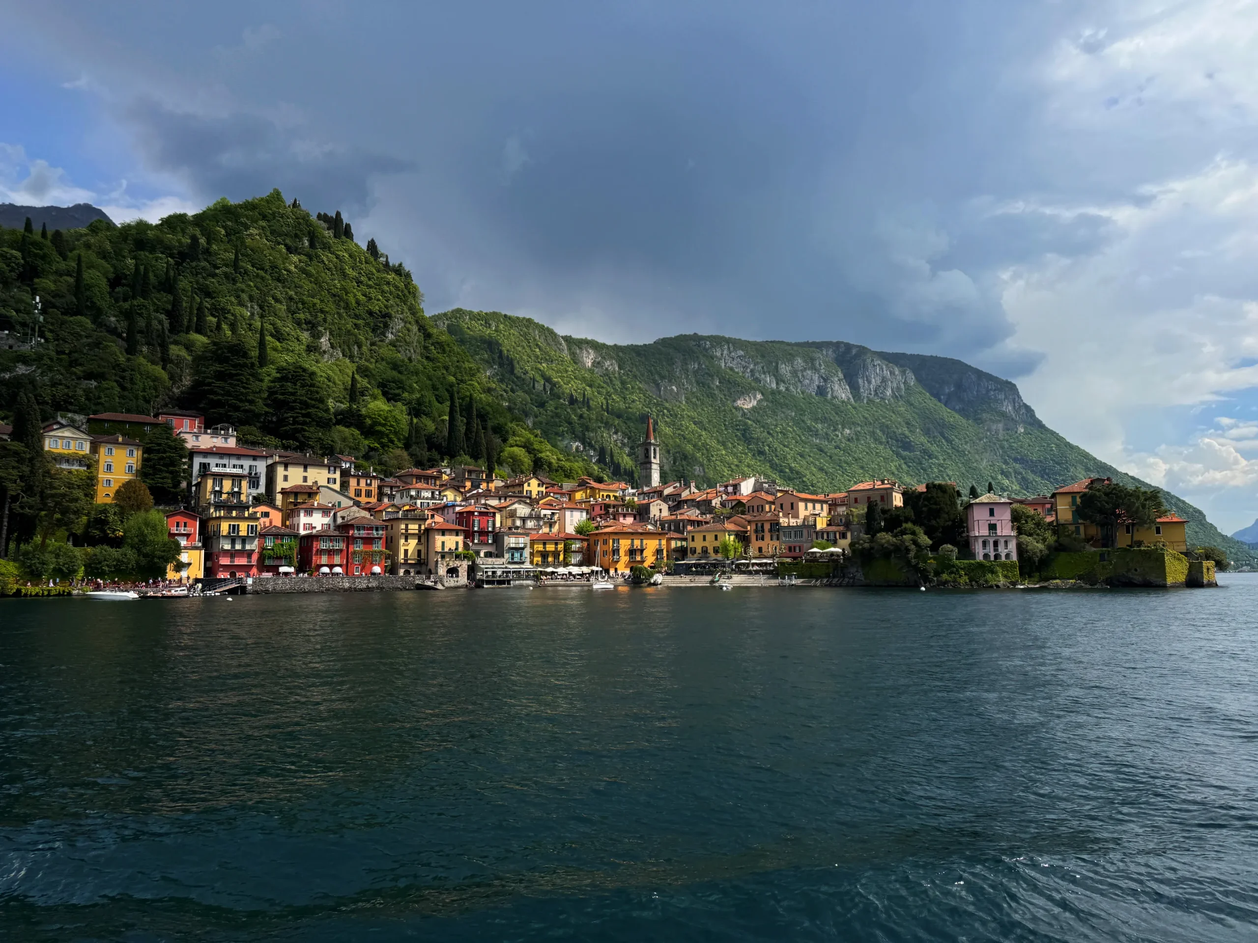 Barevné domky městečka Varenna stoupající nad břehem jezera Como, zvonice a lodě na vodě