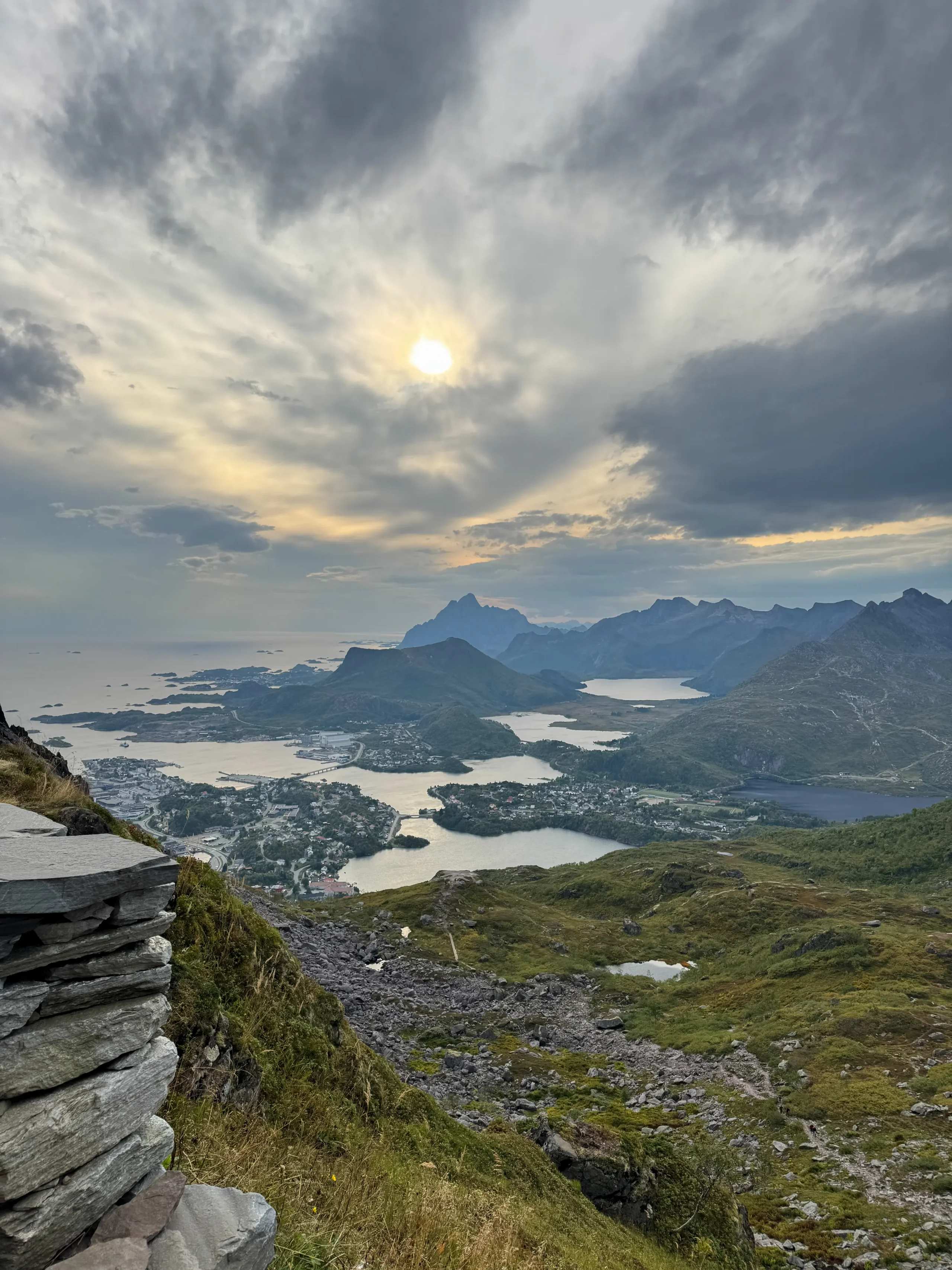 Výhled z Djevelportenu na Svolvær a fjordy Lofot při dramatické oblačnosti se sluncem prosvítajícím mezi mraky