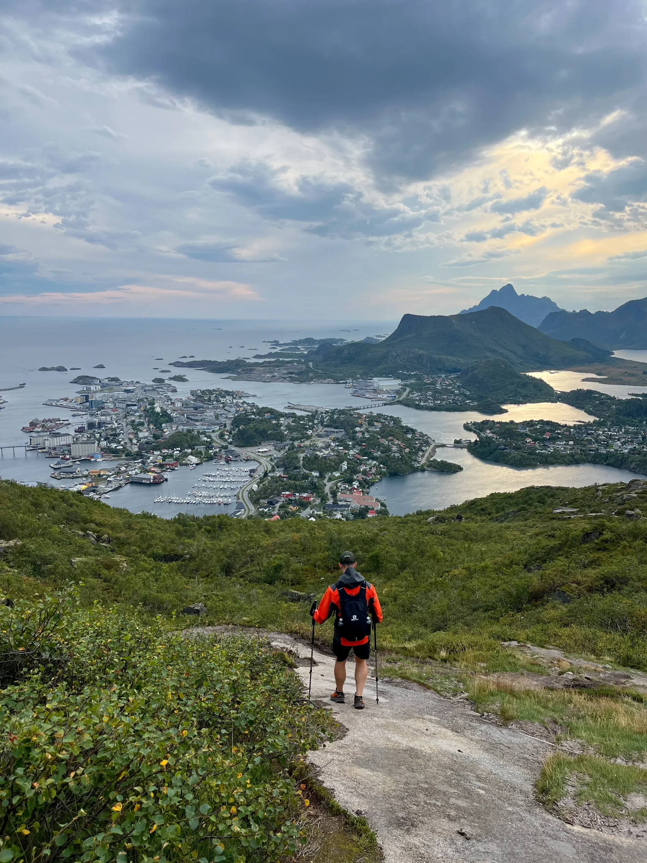 Turista s hůlkami a batohem na trase na Djevelporten s panoramatem Svolværu v pozadí