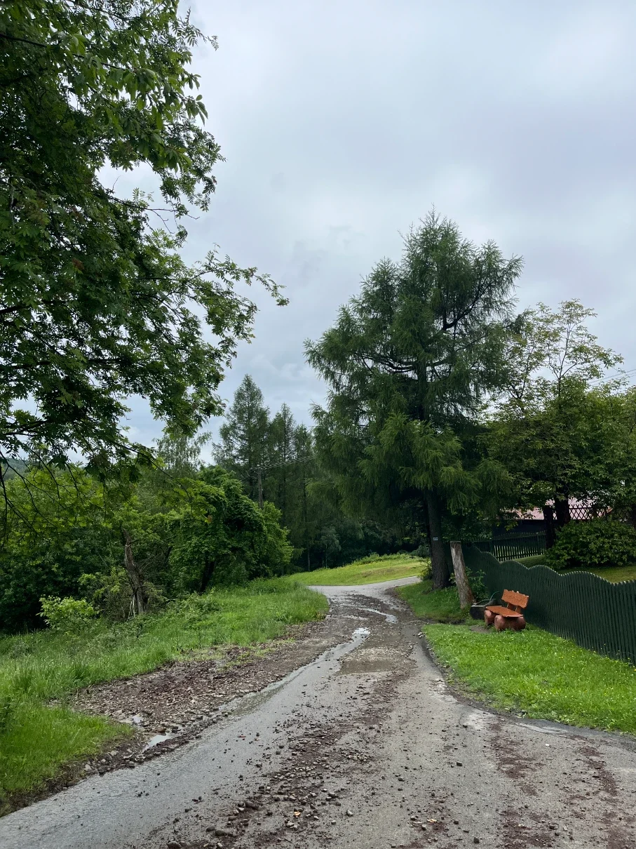 Muddy gravel road with puddles after rain and a wooden bench by a green fence in the Hołcyna Valley near Brenna