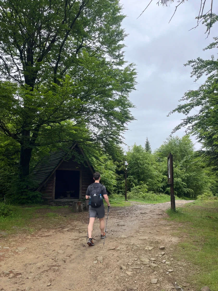 Hiker with backpack approaching the wooden log shelter at the trail junction near the Kotarz summit