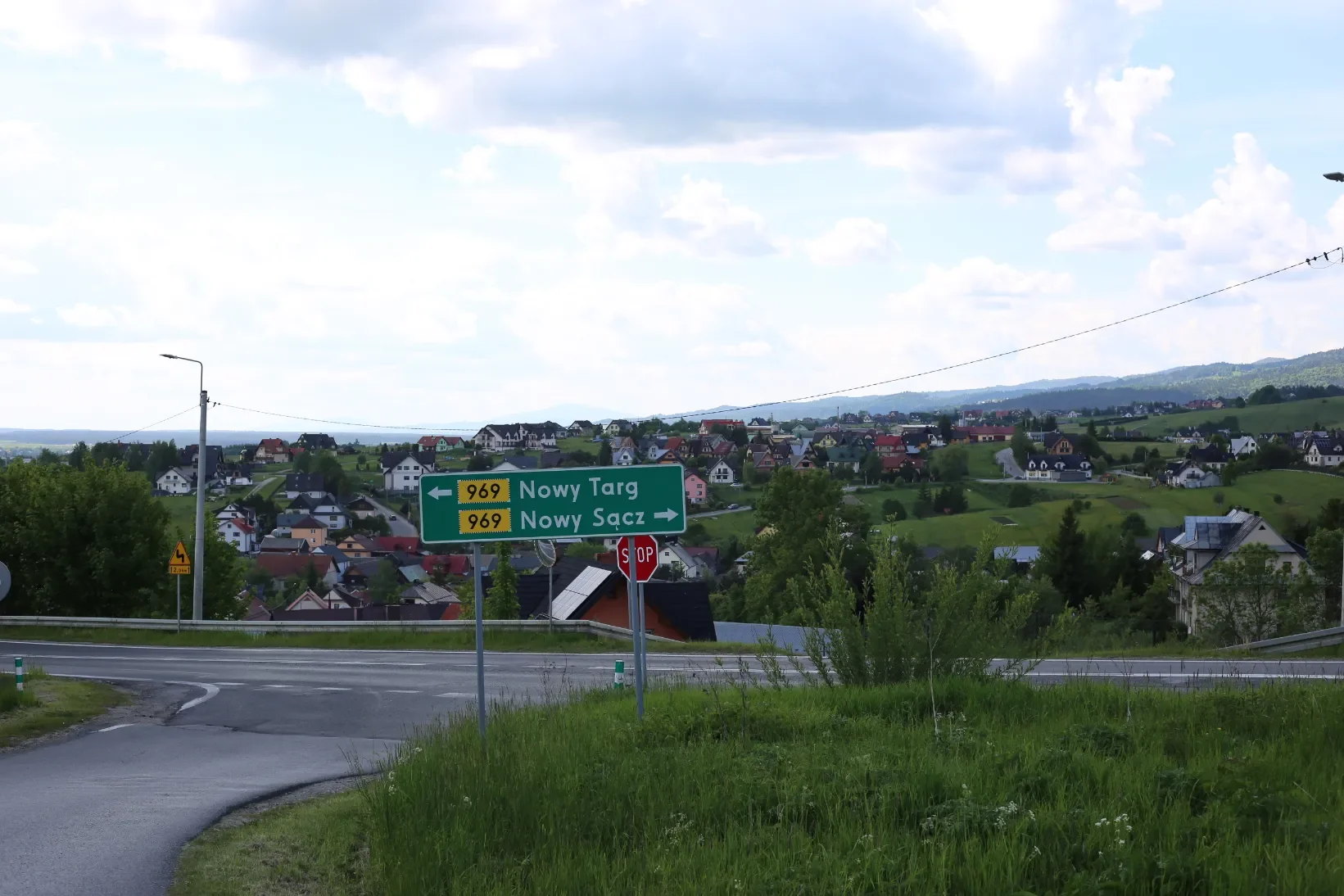 Rozcestník u silnice 969 do Nowého Targu a Nowého Sącze na pozadí vesnice rozložené na kopcích, sestup po žluté značce