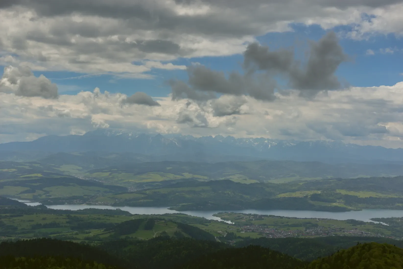 Panorama z Lubani na Czorsztyńské jezero a zamlžený hřeben Vysokých Tater na obzoru pod mraky