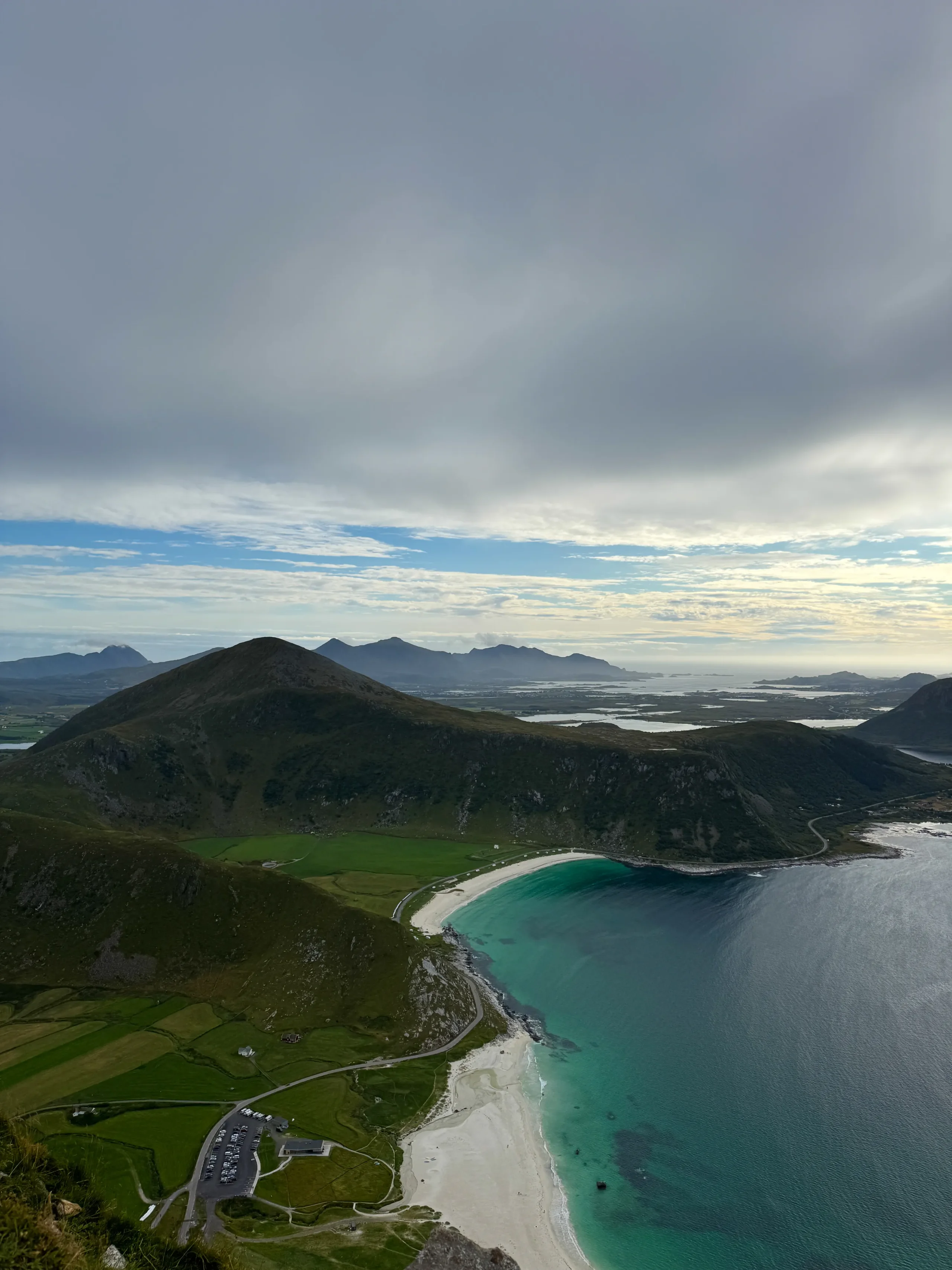 Panorama z vrcholu Mannen na pláže Haukland a Uttakleiv a lofotské vrcholy v mracích