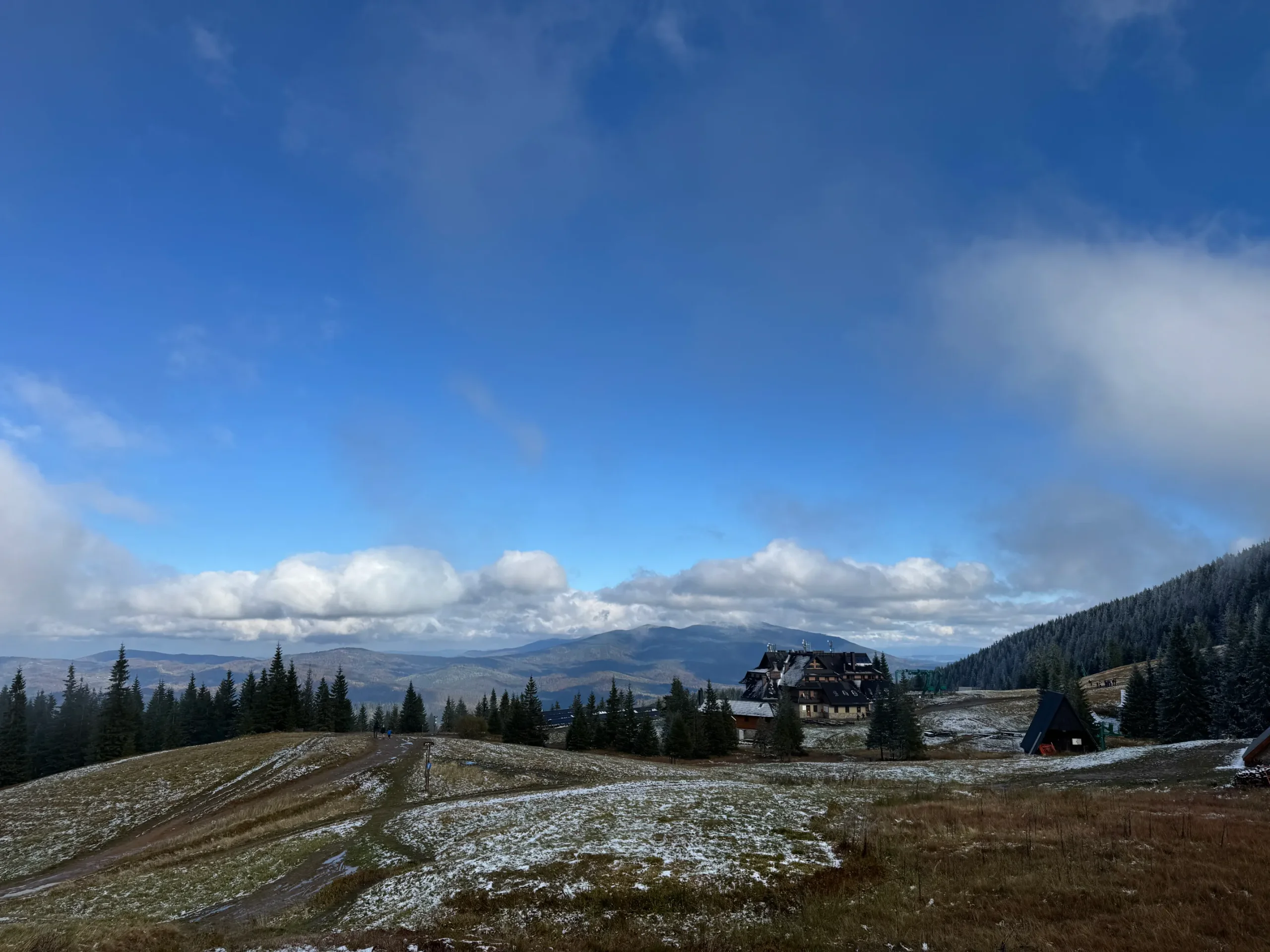 Hala Miziowa s prvním sněhem, budovou chaty a rozlehlým panoramatem Beskyd s Babí horou na obzoru