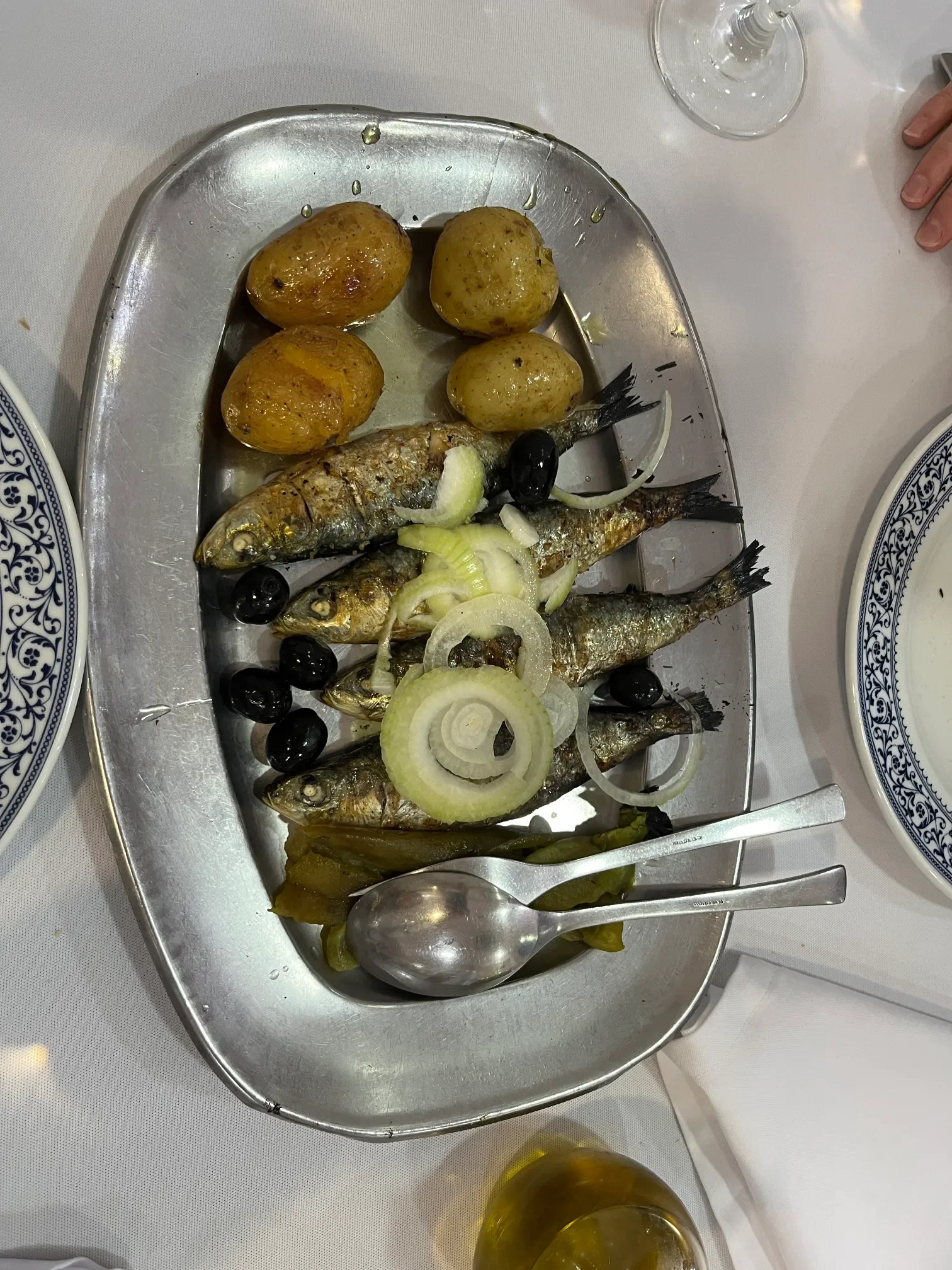 Grillowane sardynki z gotowanymi ziemniakami, czarnymi oliwkami i krążkami cebuli na metalowym półmisku w Porto