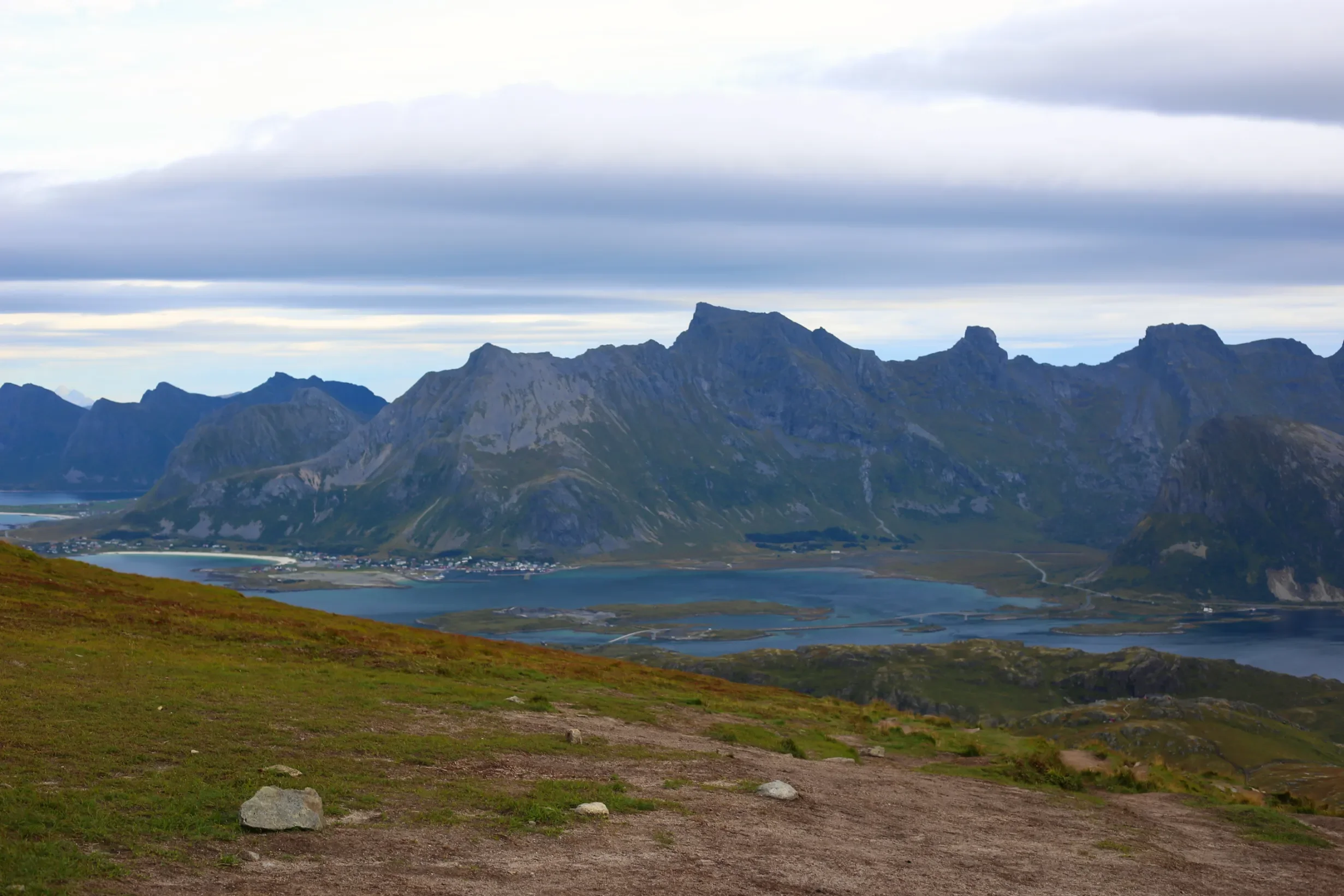 Panorama z vrcholu Ryten na fjordy Lofot a pláž Ramberg pod zataženou oblohou