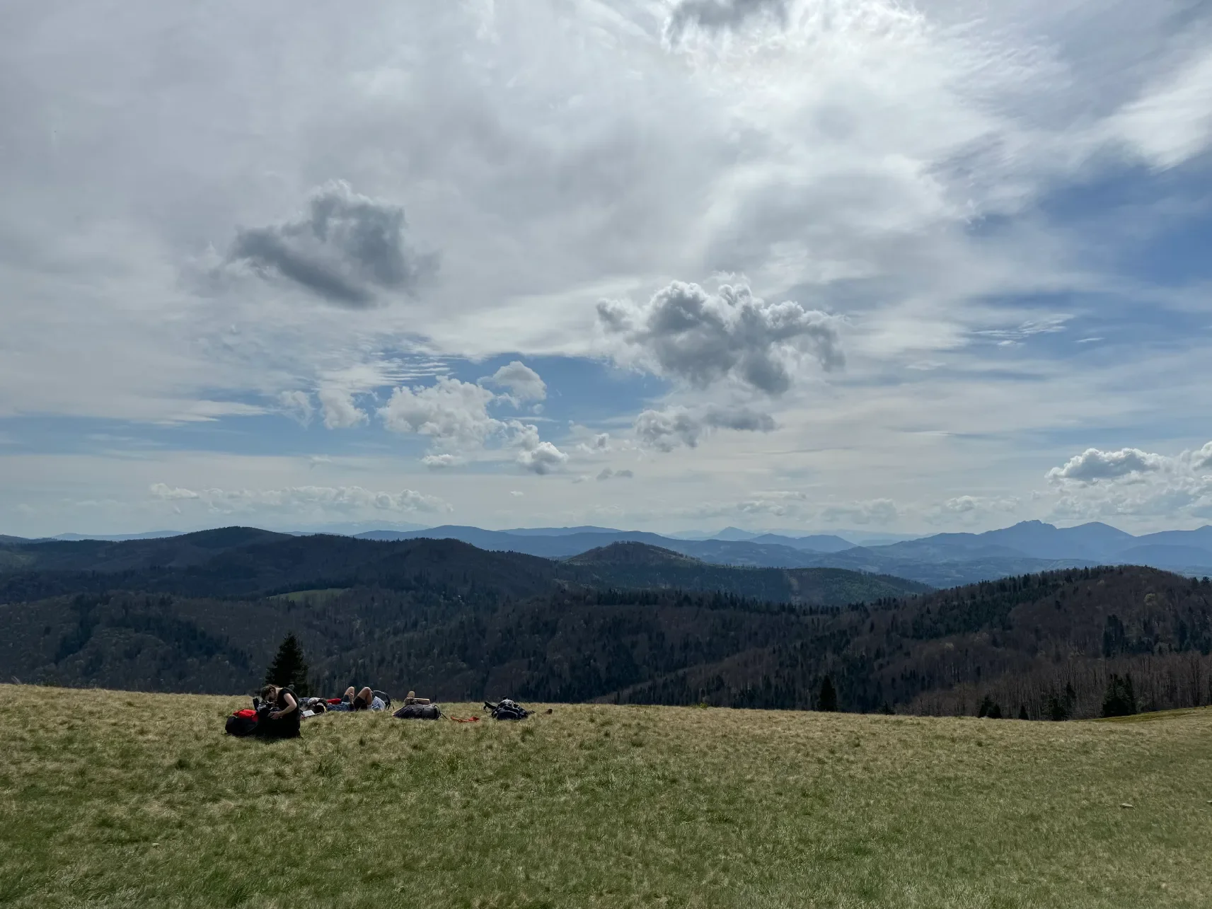 Turisté odpočívající na horské louce s velkolepým panoramatem Beskyd na trase přes Przegibek